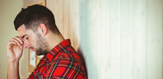 Man leaning against a wall and looking distressed